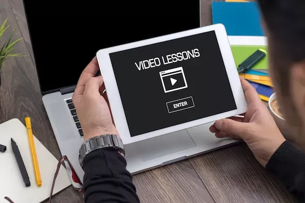 Person holding tablet displaying video lessons interface.