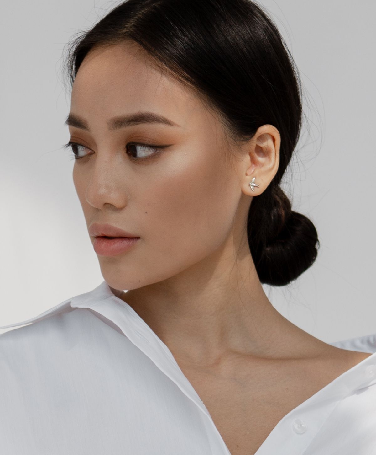Woman in white shirt, elegant hairstyle and earrings.