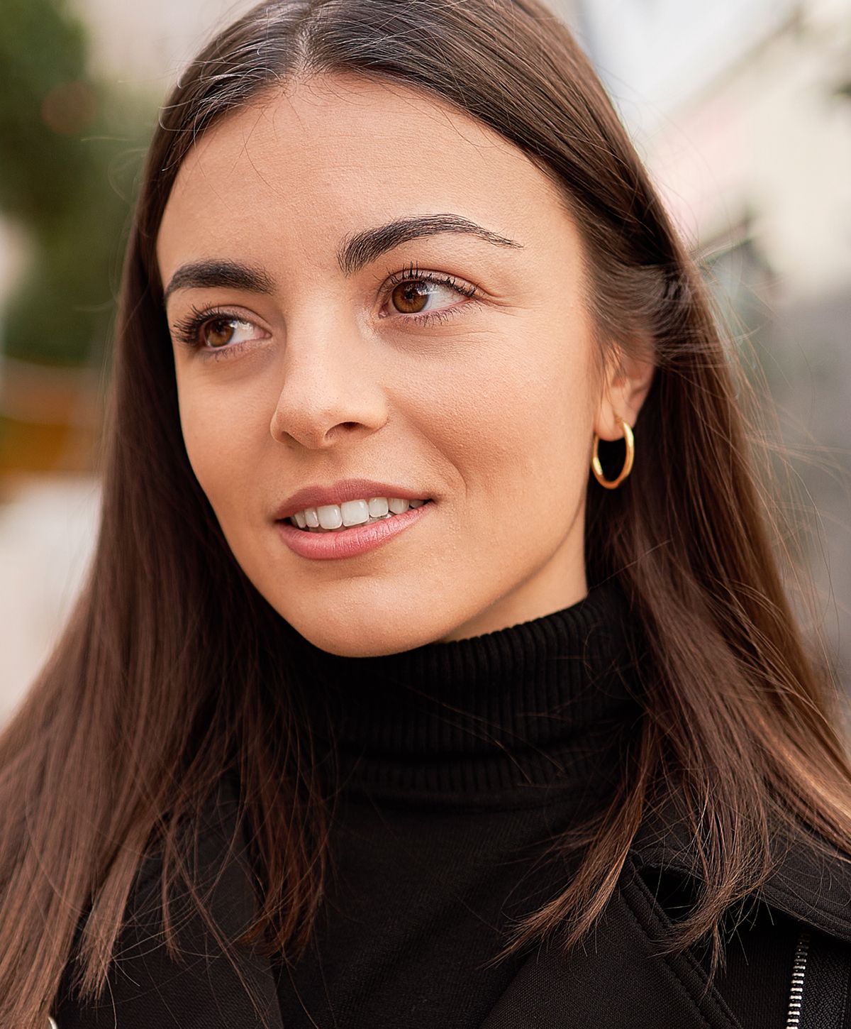 Smiling woman in a black turtleneck, outdoor setting.