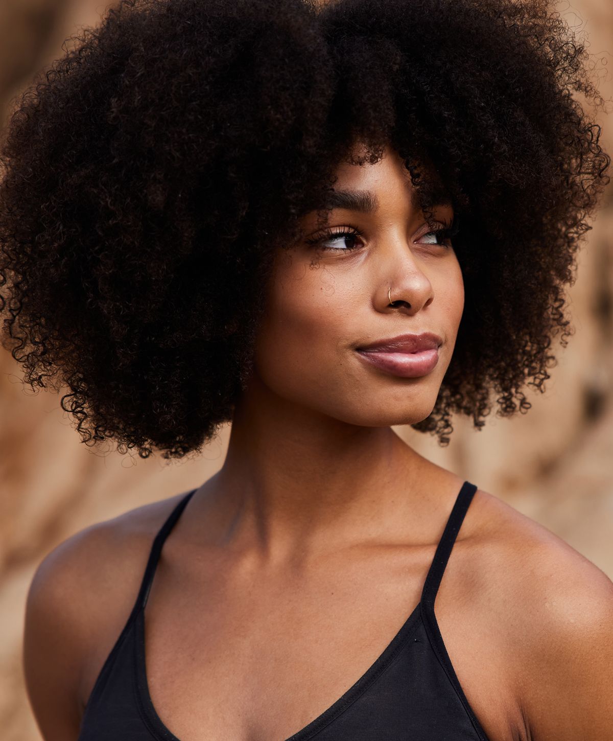 Woman with curly hair outdoors, looking thoughtfully.