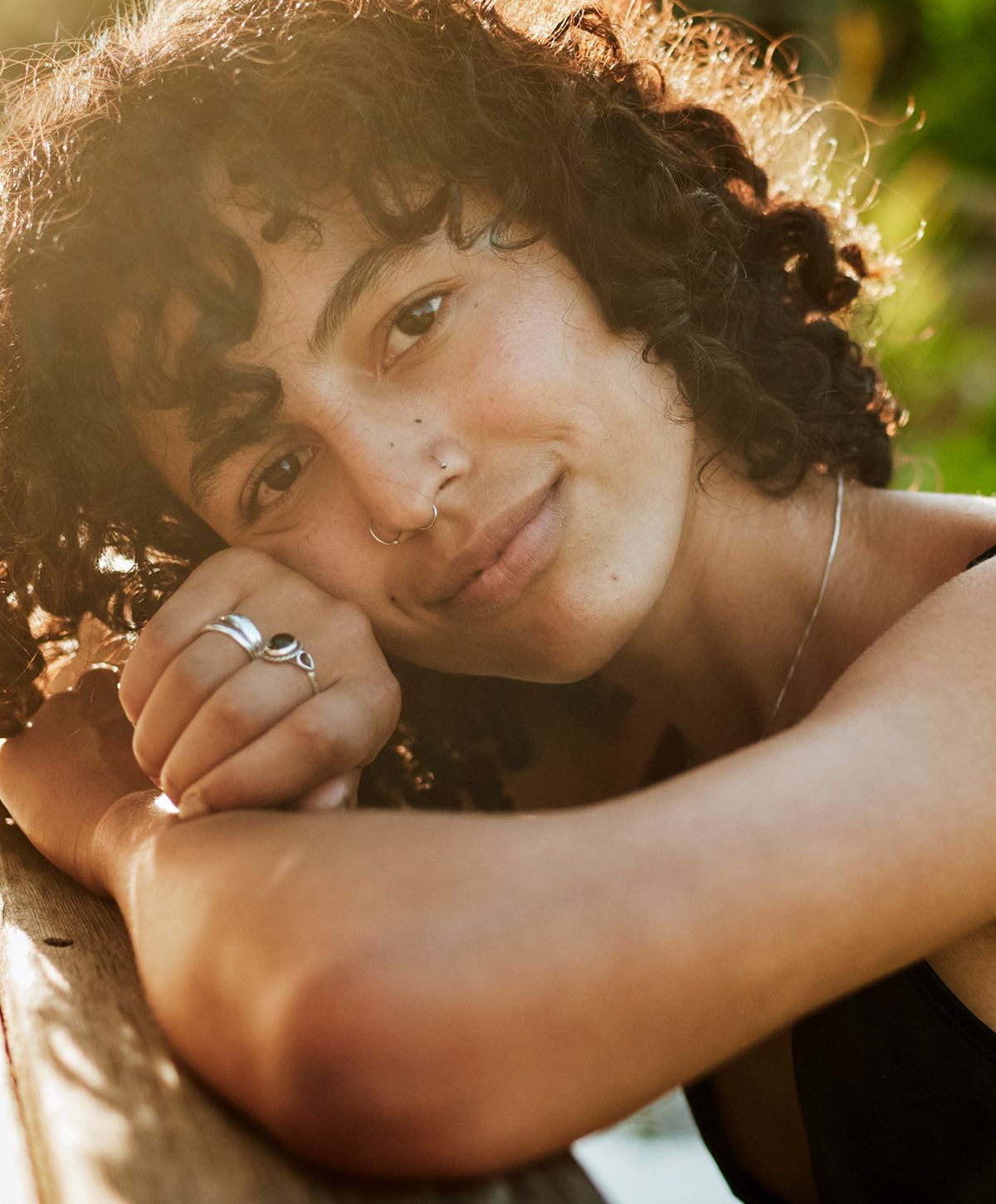 Smiling person with curly hair resting on arm.