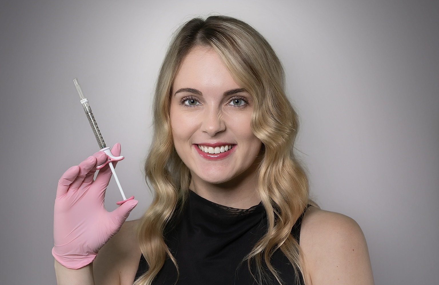 Woman smiling with syringe and pink gloves.