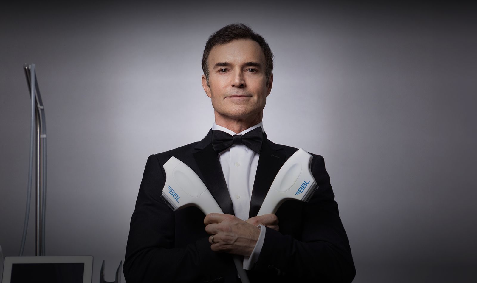 Man in tuxedo holding beauty equipment, professional setting.