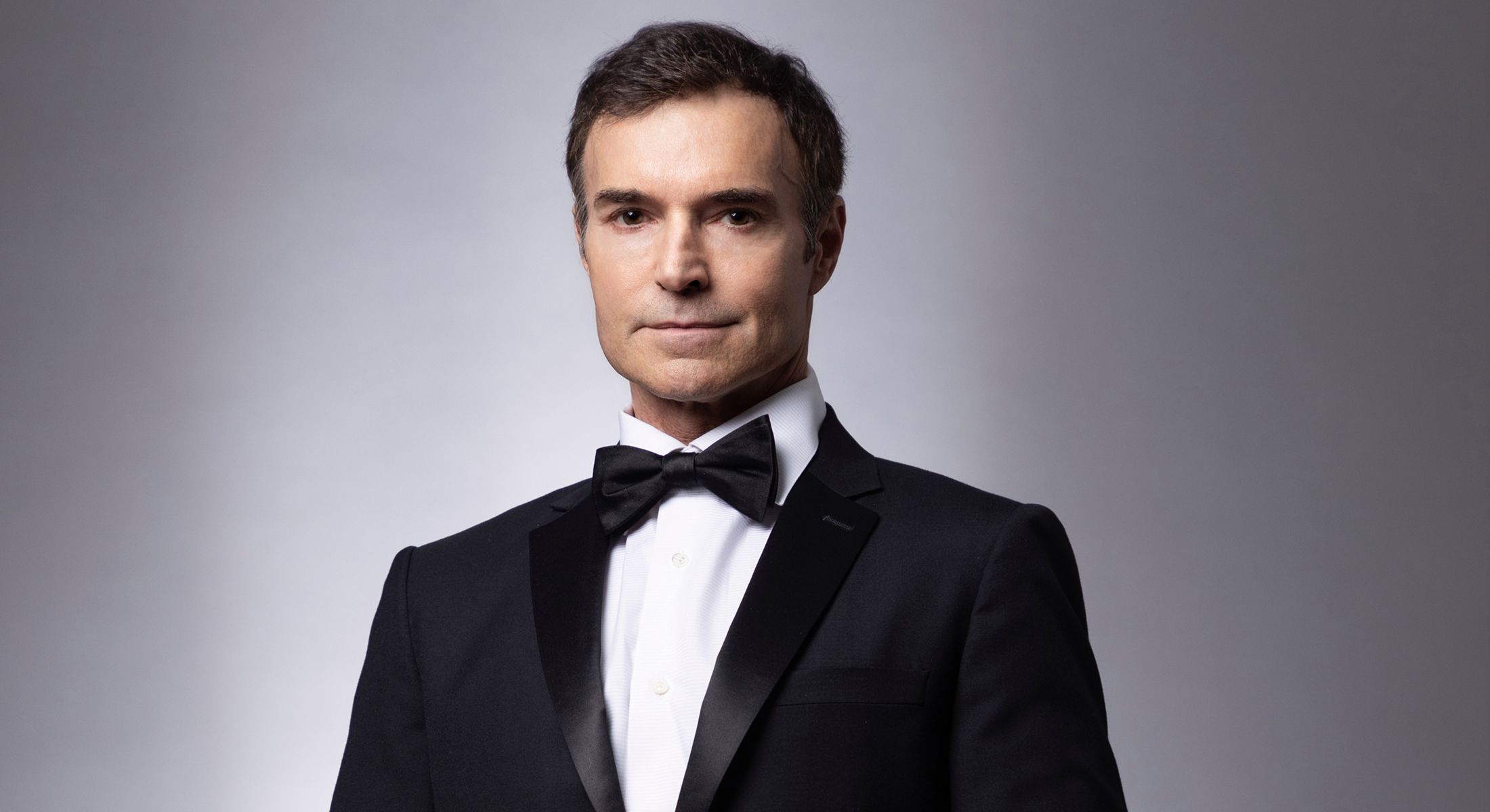 Man in tuxedo with bow tie, serious expression.