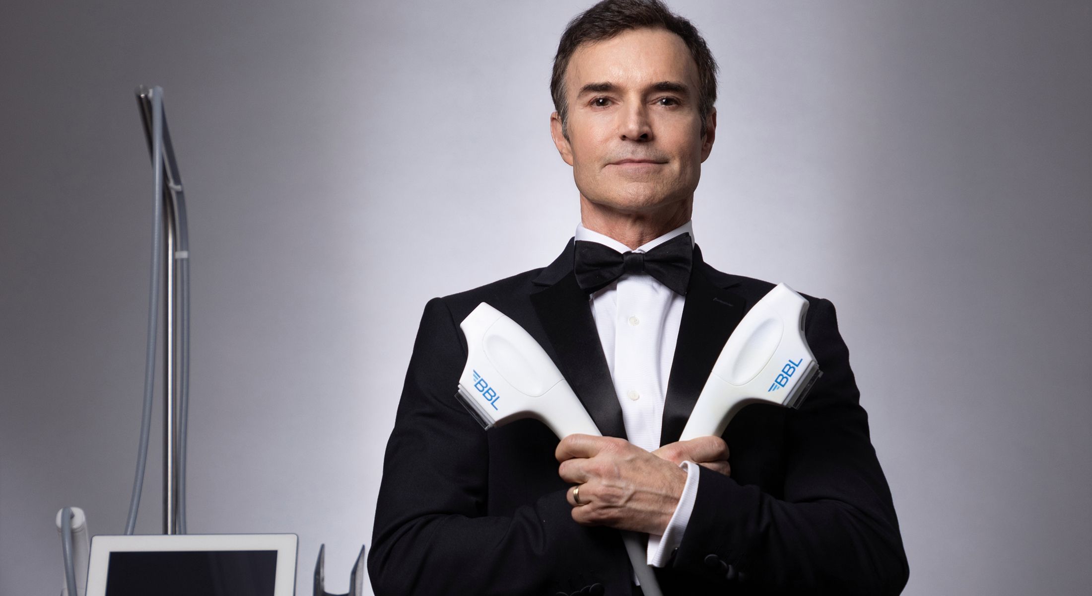 Man in tuxedo holding advanced beauty technology devices.