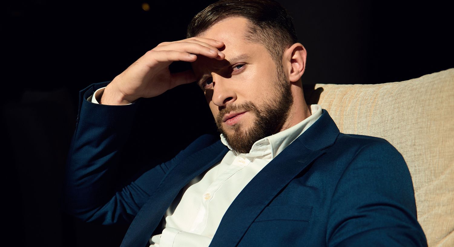 Man in suit thoughtfully resting hand on forehead.